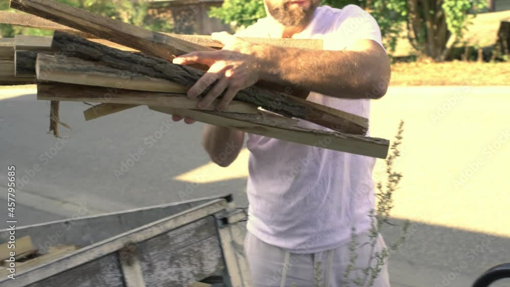 Close up right, man taking wood from tow to hand truck, morning sun light Close up right, man taking wood from tow to hand truck, morning sun light