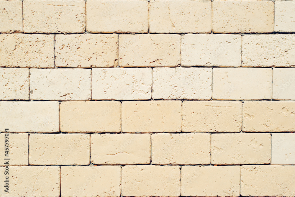 Obraz premium Rough decorative light yellow large brick, textured stone wall outdoors background. Structural beige material for exterior wall decoration