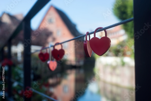 Closeup of red padlocks in shaped heart on metallic cable in border water © pixarno