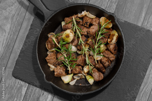 Diced Aberdeen Angus beef with shallots and rosemary, fried in a cast iron frying pan. Selective colour image
