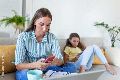 young mom working at home with her child on the sofa while writing an email. Young woman working from home, while in quarantine isolation during the Covid-19 health crisis