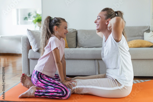 Cheerful young woman and little girl in sportswear exercising together in modern light room. mother and daughter practicing yoga