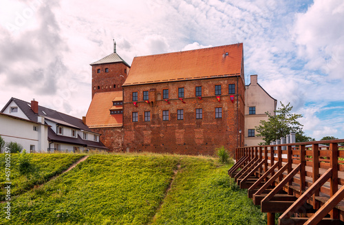 view of the gothic castle of Pomeranian dukes in Dar  owo. A moat and a bridge in the foreground. The walls of the castle are made of red brick and the roof is covered with tiles