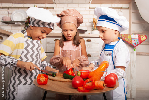 small children in cook costumes in a cap and apron prepare a salad of their fresh vegetables for vegan day, cook's day or mother's day