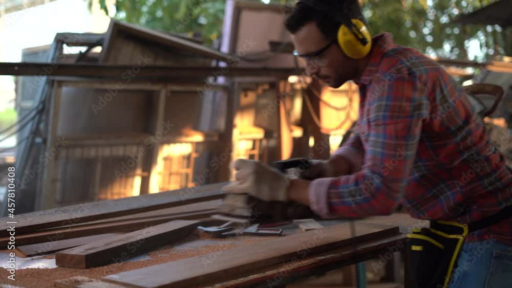 carpenter wearing Safety Glasses and Protective ear muffs using electric wood plane with plank in wood working factory carpenter wearing Safety Glasses and Protective ear muffs using electric wood plane with plank in wood working factory