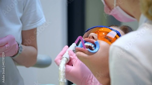 Dentist And Assistant Applies Whitening Gel To Patient's Teeth. Teeth Whitening In a Dental Clinic. Healthcare And Medicine Concept. Close Up