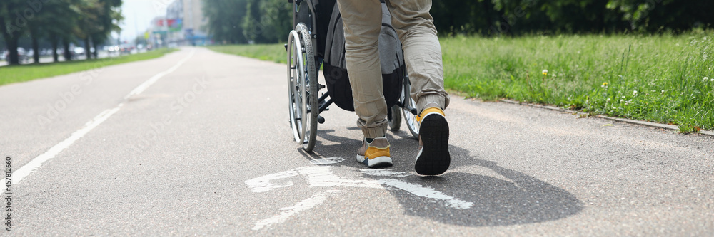 Man helping disabled person in wheelchair to walk on sidewalk