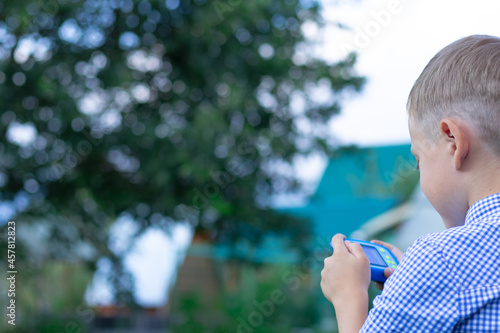 A cute preschool boy with a neat hairstyle in a blue shirt takes pictures of green plants on a hot summer day. Selective focus. Portrait