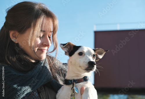 young woman holding jack russel terrier dog while it looking aside. happy dog with owner outdoors. city walking with pet