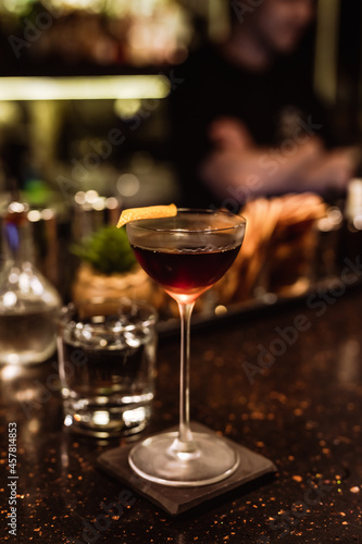 A classic Manhattan cocktail garnished with an orange zest in a beautiful glass at the bar