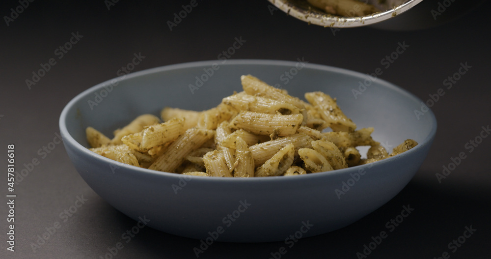 pesto penne fall into blue bowl on black background