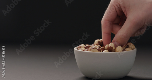 man hand take roasted hazelnuts from white bowl on black background