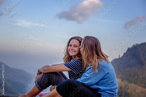 Beautiful happy lesbian couple sitting and hugging with mountain view, tenderness and love concep