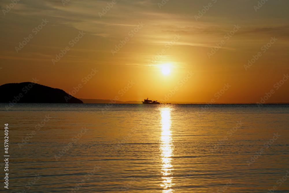 Bright red sunset over the Aegean Sea. Sun and mountains. Skyline and silhouette of the ship. Waves and glare.