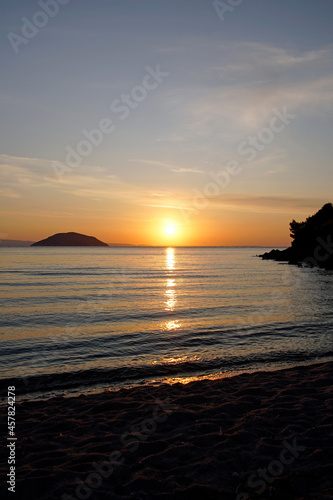 Bright red sunset over the Aegean Sea. Sun and mountains. Horizon. Waves and glare. Beach. Vertical shot