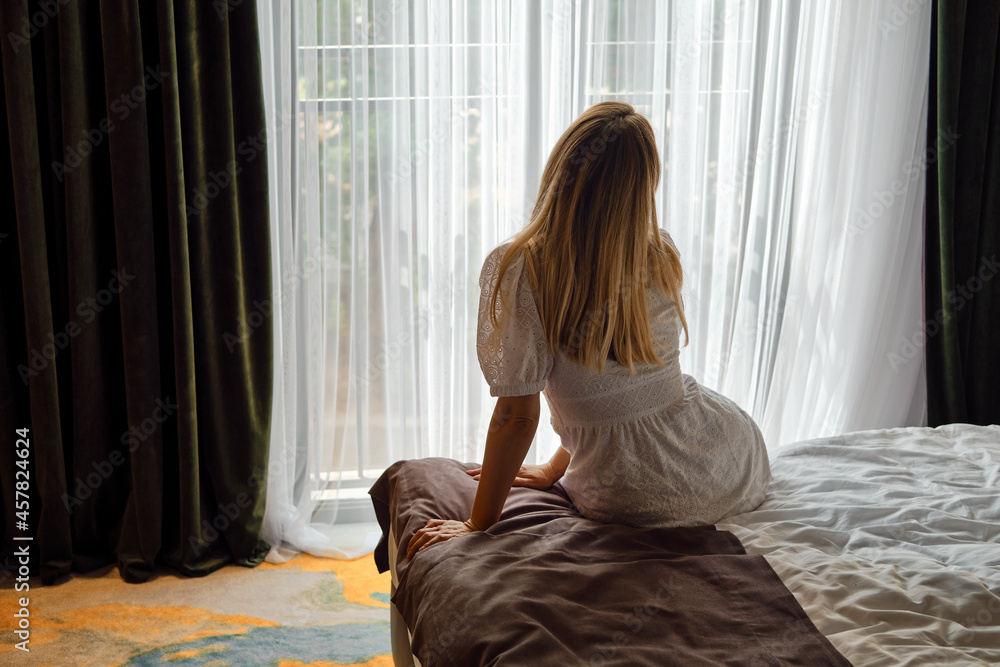 A girl in a white dress stretches after getting out of bed and looking out the window. Morning rituals for a vigorous workday. Health and relaxation concept A girl in a white dress stretches after getting out of bed and looking out the window. Morning rituals for a vigorous workday. Health and relaxation concept