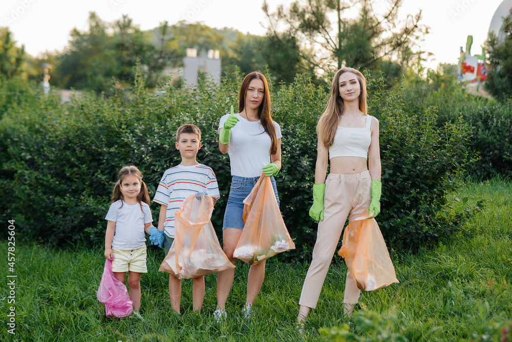 Fototapeta premium A group of girls with children at sunset are engaged in garbage collection in the park. Environmental care, recycling.