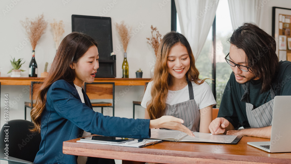 Cheerful Asian small business owners couple meeting with consultant talking about business plan and finance in cafe. Young Japanese agent consider signing contract insurance together at restaurant. Cheerful Asian small business owners couple meeting with consultant talking about business plan and finance in cafe. Young Japanese agent consider signing contract insurance together at restaurant.