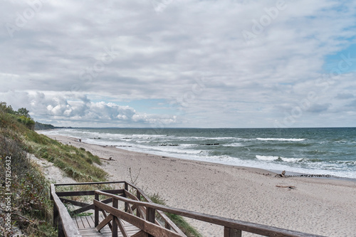 Beautiful seascape with waves  sandy beach  old breakwaters  cloudy sky and wooden stairs in foreground.