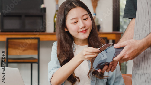 Young Asian freelance women pay contactless credit card at coffee shop. Asian happy men barista waiter wear gray apon holding credit card reader machine for customer can pay with technology in cafe. photo