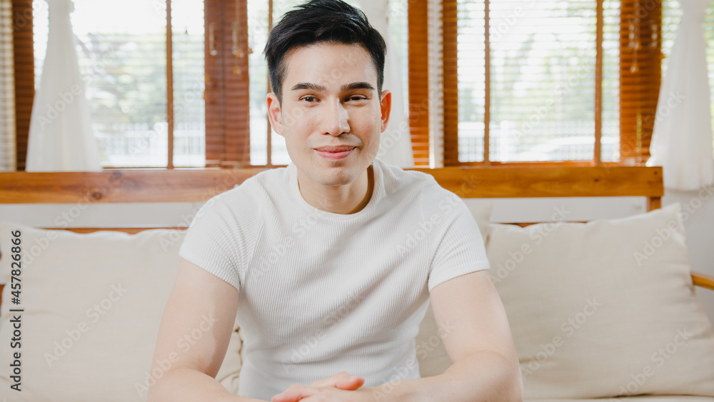 Happy young freelance asia man looking at camera smiling and cheerful relax on video call online on sofa in living room at home, Stay at house quarantine, work from home, Social distancing concept. Happy young freelance asia man looking at camera smiling and cheerful relax on video call online on sofa in living room at home, Stay at house quarantine, work from home, Social distancing concept.
