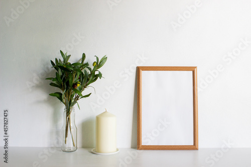 A frame with candles and leaves on a white wall with nature light. 