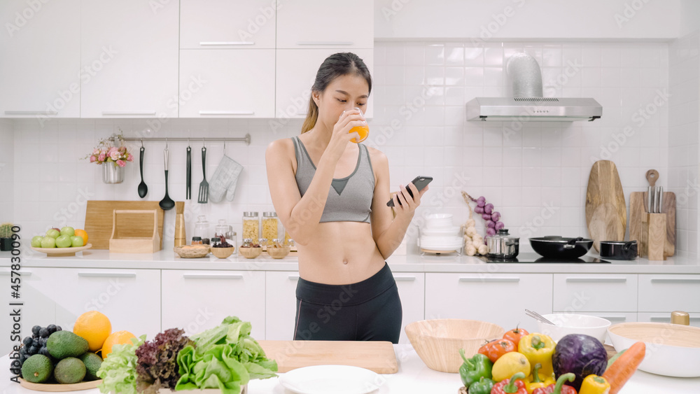 Young Asian blogger woman using smartphone for talking, chatting and checking social media in the kitchen, female in sport clothing cooking at home. Lifestyle women relax at home concept.