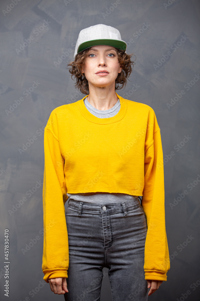 Autumn mood! Portrait of happy smiling woman with short brunette curly hair wearing yellow sweater and a hat over grey wall background Autumn mood! Portrait of happy smiling woman with short brunette curly hair wearing yellow sweater and a hat over grey wall background