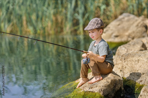 little boy sitting on stone and fishing