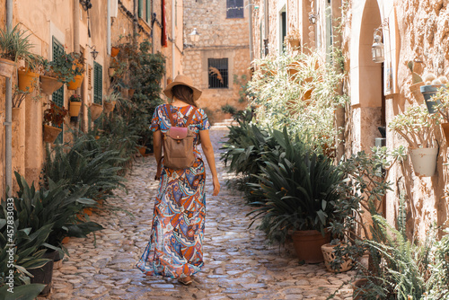 A women tourist seen in the background walks a cozy and beautiful street decorated with flower in Valldemossa, Mallorca, Spain. Holidays in Spain photo