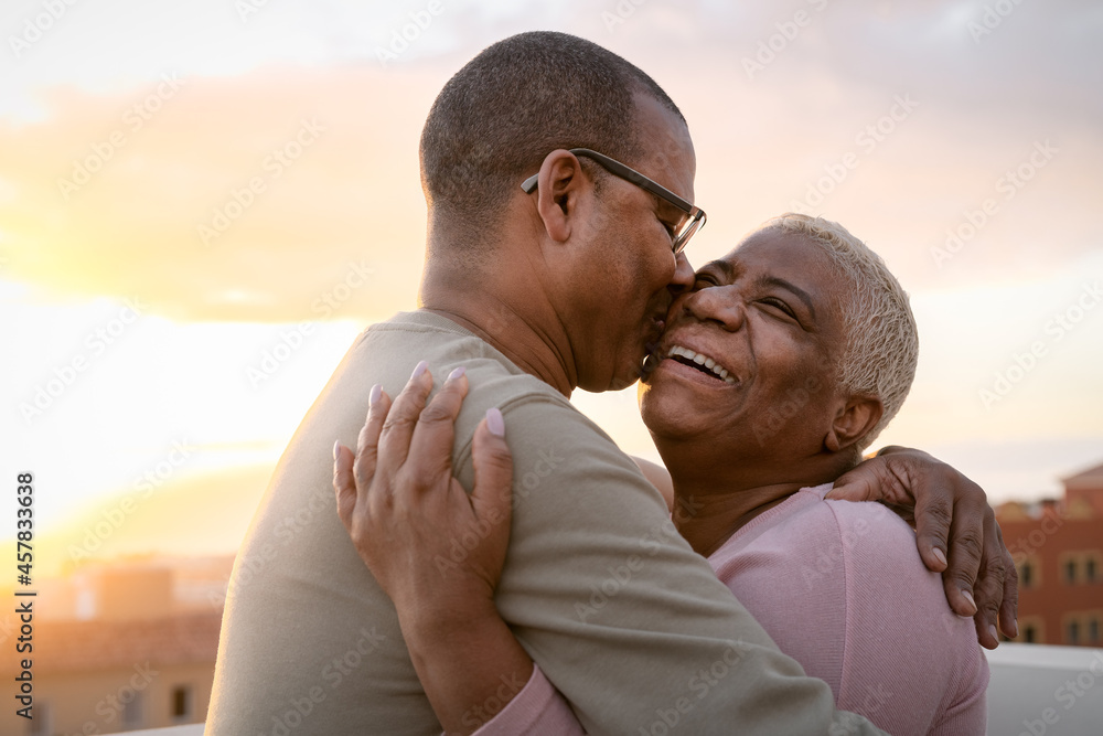 Happy Latin senior couple having romantic moment embracing on rooftop during sunset time - Elderly people love concept - obrazy, fototapety, plakaty 