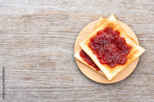 Toast sliced bread with red jam in wooden plate isolated on wooden table background. Top view. Flat lay. 