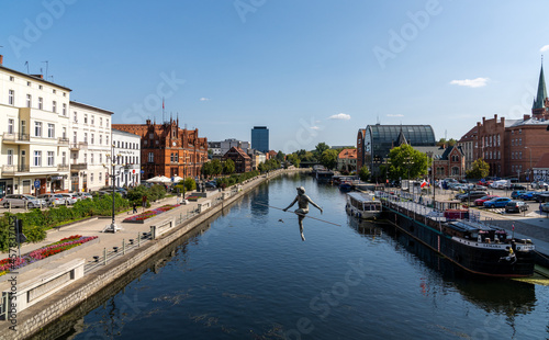 view of the historic waterfront warehouses and buildings on the Brda River in downtown Bygdoszcz with the Crossing the River sculpture in the foreground