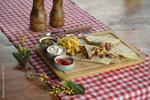 Closeup of quesadilla steaks with mushrooms, french fries, and sauces on a board on the table