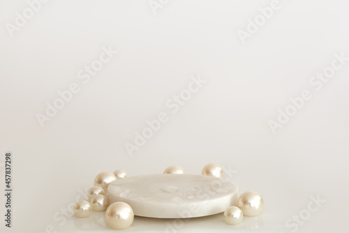 White marble podium with pearls and water drops on the white background. Podium for product, cosmetic presentation. Creative mock up. Pedestal or platform for beauty products.