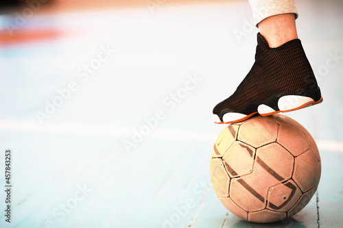 A human foot rest on the football on the concrete floor. Photo of one soccer ball and sneakers in a wooden floor.