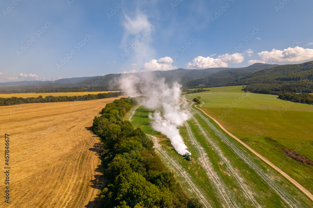 Aerial view of a tractor spreading lime on agricultural fields to improve soil quality after the autumn harvest. The use of lime powder to neutralize the acidity of the soil.