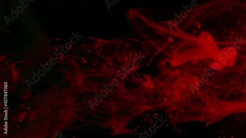 Red watercolor ink in water on a black background. Meditative abstract background. Screensaver, relaxing space background. Slow motion of colored watercolors in water.