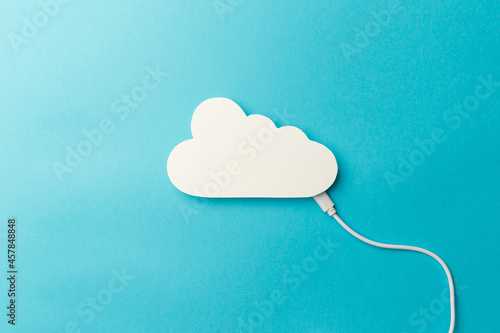 The concept of cloud technologies, cloud storage. A white cable is connected to a cloud on a blue background. Top view. Flat lay. Close-up. Copy space. Transferring data to cloud storage