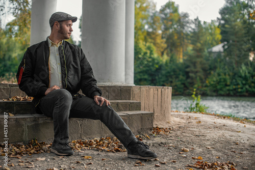 a serious man in black sits on the steps in the autumn by the river in a park