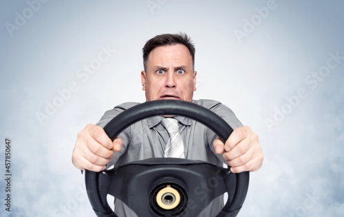 Scared man with open mouth holding car steering wheel, on light blue smoke background, front view.  