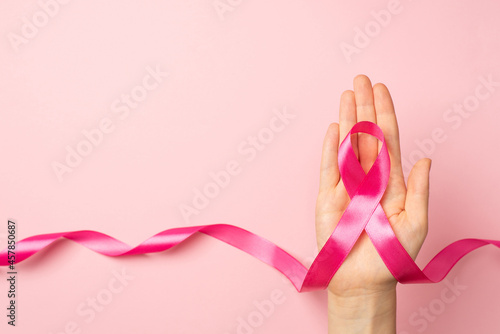 Photographie First person top view photo of female hand holding pink ribbon in palm symbol of