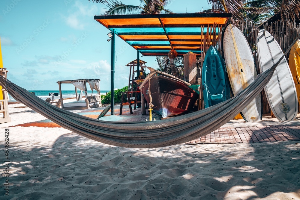 Hanging empty hammock with boat and canoe on sand at beautiful Mexican beach resort