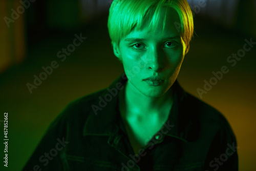 portrait of a strange girl with short blonde hair who looks straight into the camera. Modern shooting in neon light. High quality photo