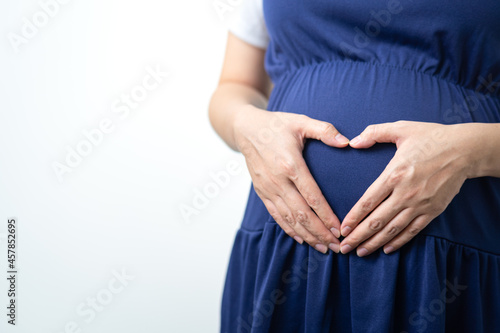 Action of hand gesture in heart icon on the pregnancy belly of mother in blue color dressing. Lovely parent emotion abstract photo. 