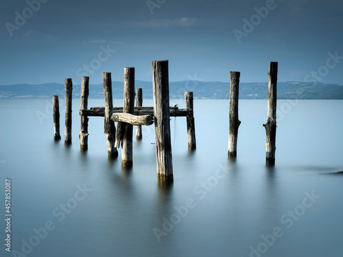 Fototapeta Naklejka Na Ścianę i Meble -  smooth water in long exposure and wooden trunk in it on lake Bolsena in Italy