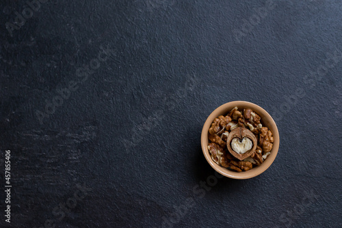 Walnut in a ceramic bowl on a dark background with copy space. View from above. In the center there is a half of a nut in the form of a heart. Ceramic plate with walnuts on a dark background. Place fo