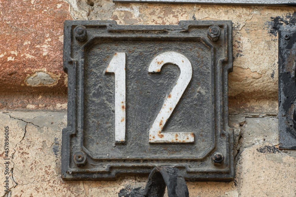 White numbers 12 on a decorative steel frame, vintage house number on the facade of an old house. White numbers 12 on a decorative steel frame, vintage house number on the facade of an old house.