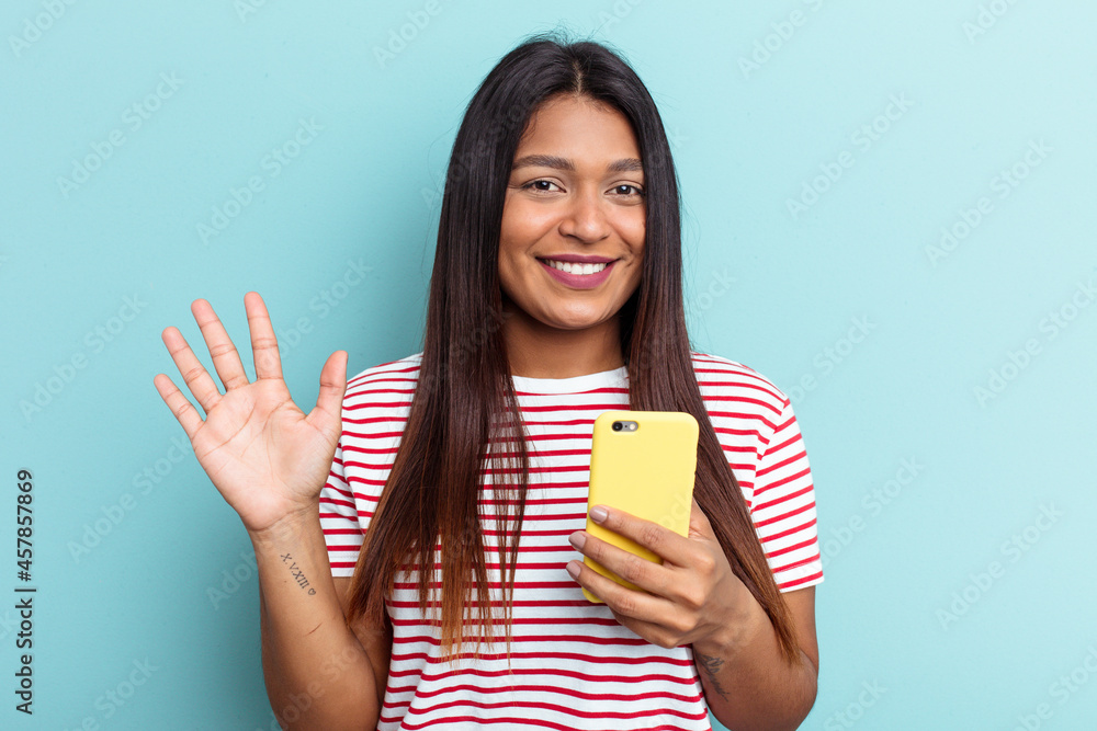 Young Venezuelan woman holding mobile phone isolated on blue background smiling cheerful showing number five with fingers. Young Venezuelan woman holding mobile phone isolated on blue background smiling cheerful showing number five with fingers.