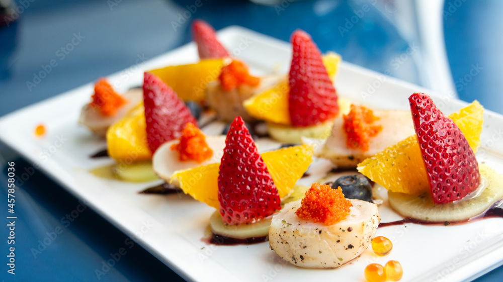Grilled scallops on a decorative plate, with fruits topping as strawberry orange and salmon roe Grilled scallops on a decorative plate, with fruits topping as strawberry orange and salmon roe